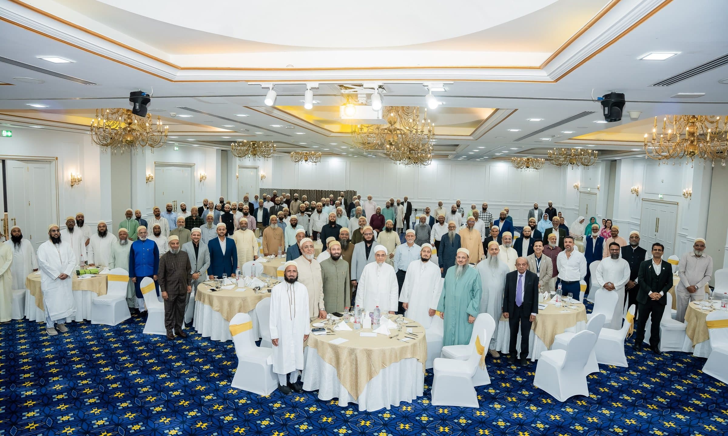 Large audience standing in a ballroom with a blue patterned carpet