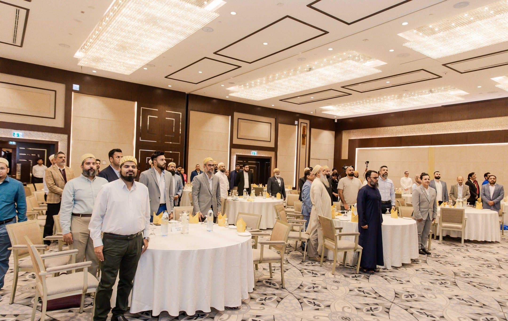 Wide view of a hotel ballroom with guests standing among round dinner tables