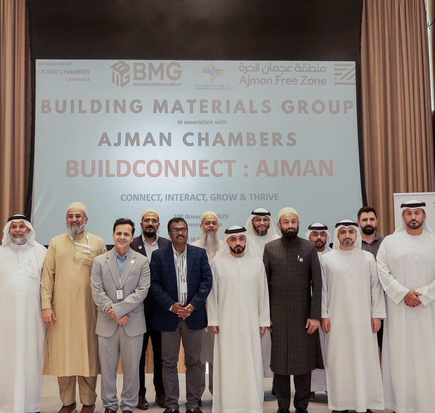 BuildConnect Ajman: Group of guests in kandura and suits posing in front of a BMG and Ajman banner