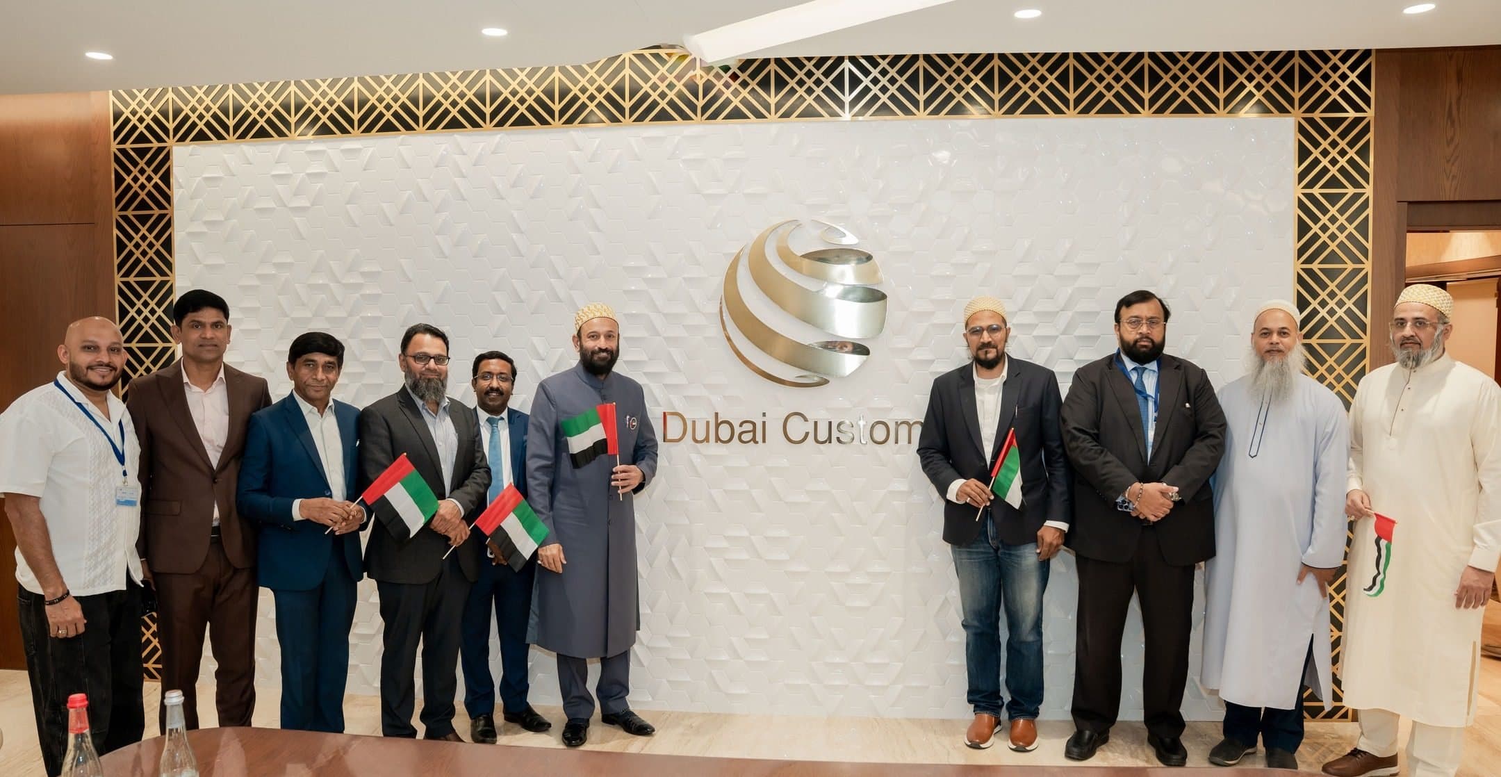 Group holding small UAE flags in front of a Dubai Customs logo wall