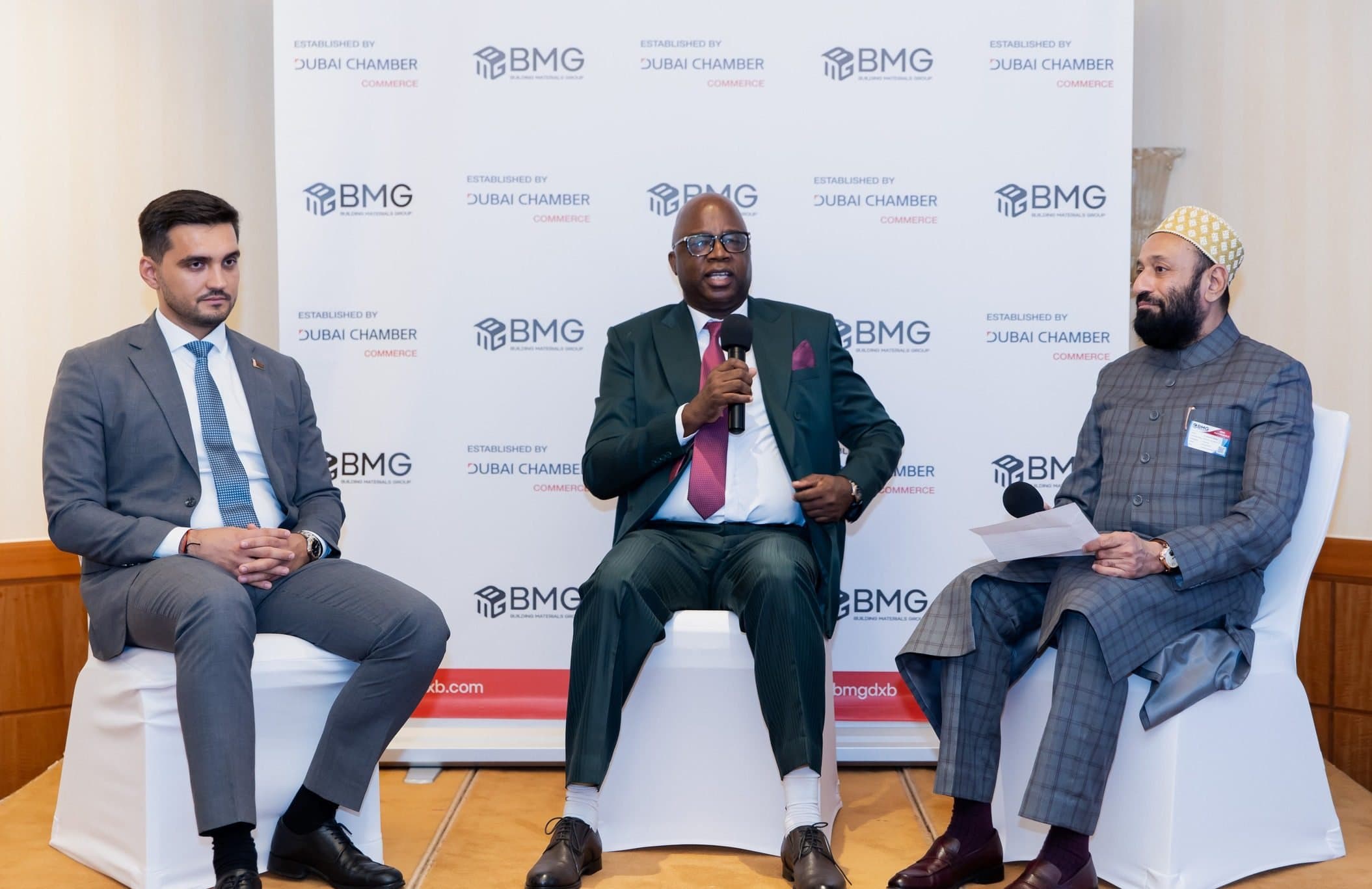 BMG FutureBuild: Innovate, Build, Grow: Three men seated on stage chairs in front of a BMG and Dubai Chamber backdrop, one speaking