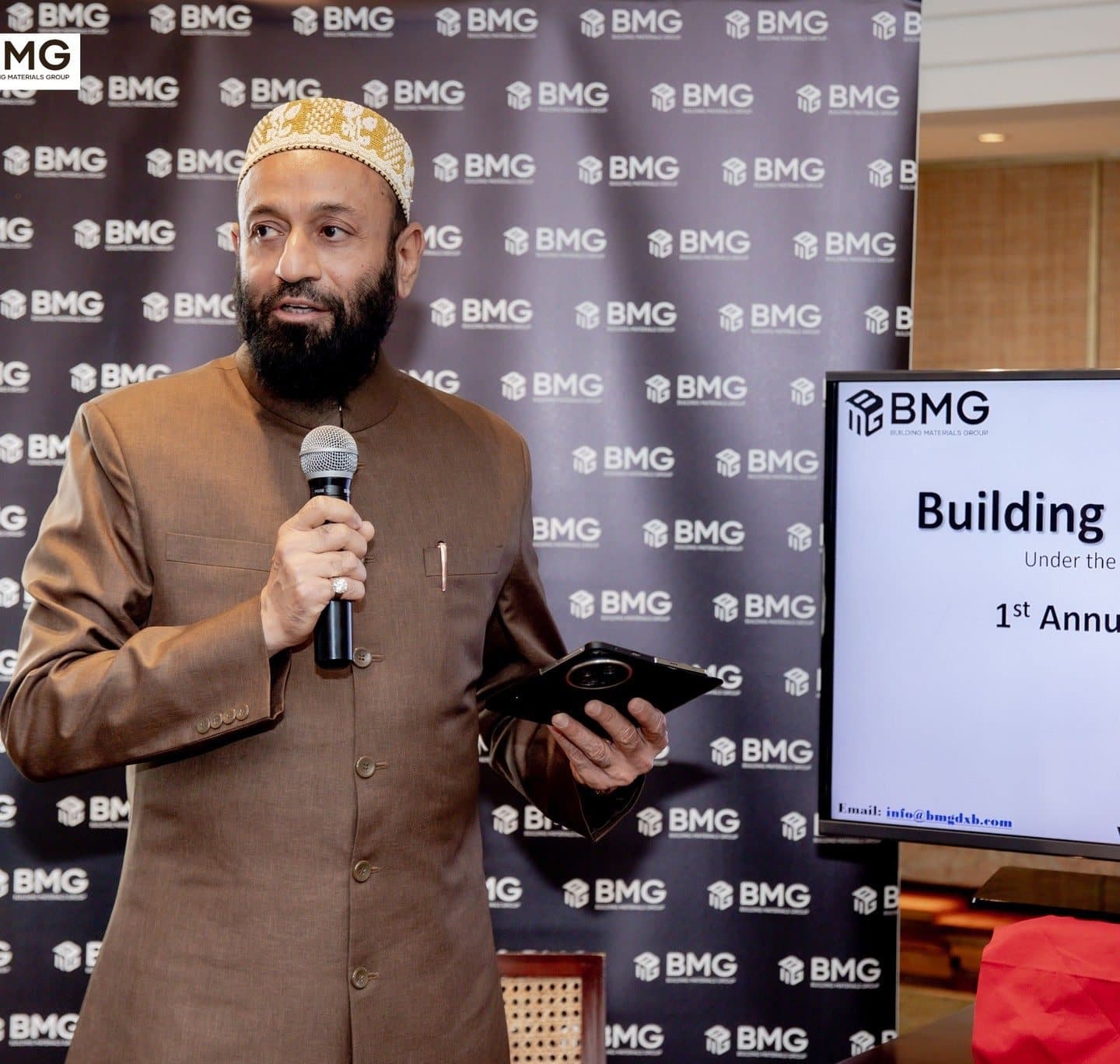 Annual General Meeting 2024: Man in a brown sherwani speaking into a microphone in front of a BMG logo wall
