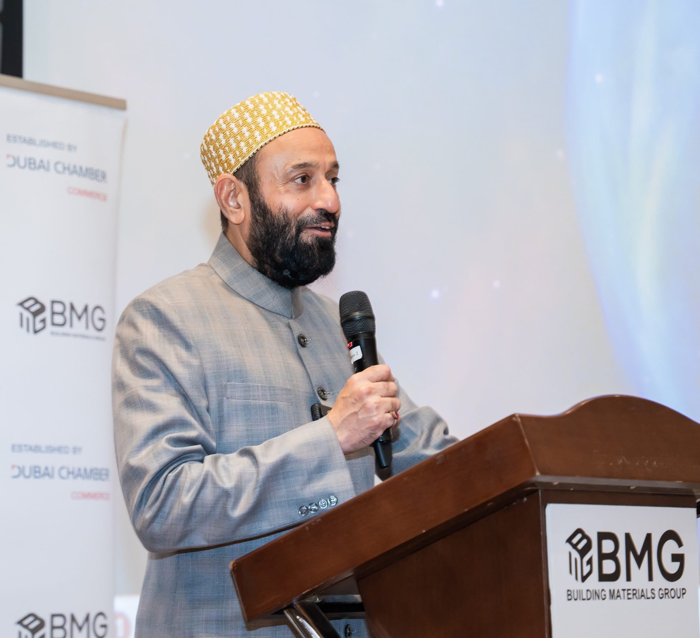 Man in a cap speaking at a BMG branded podium with a microphone