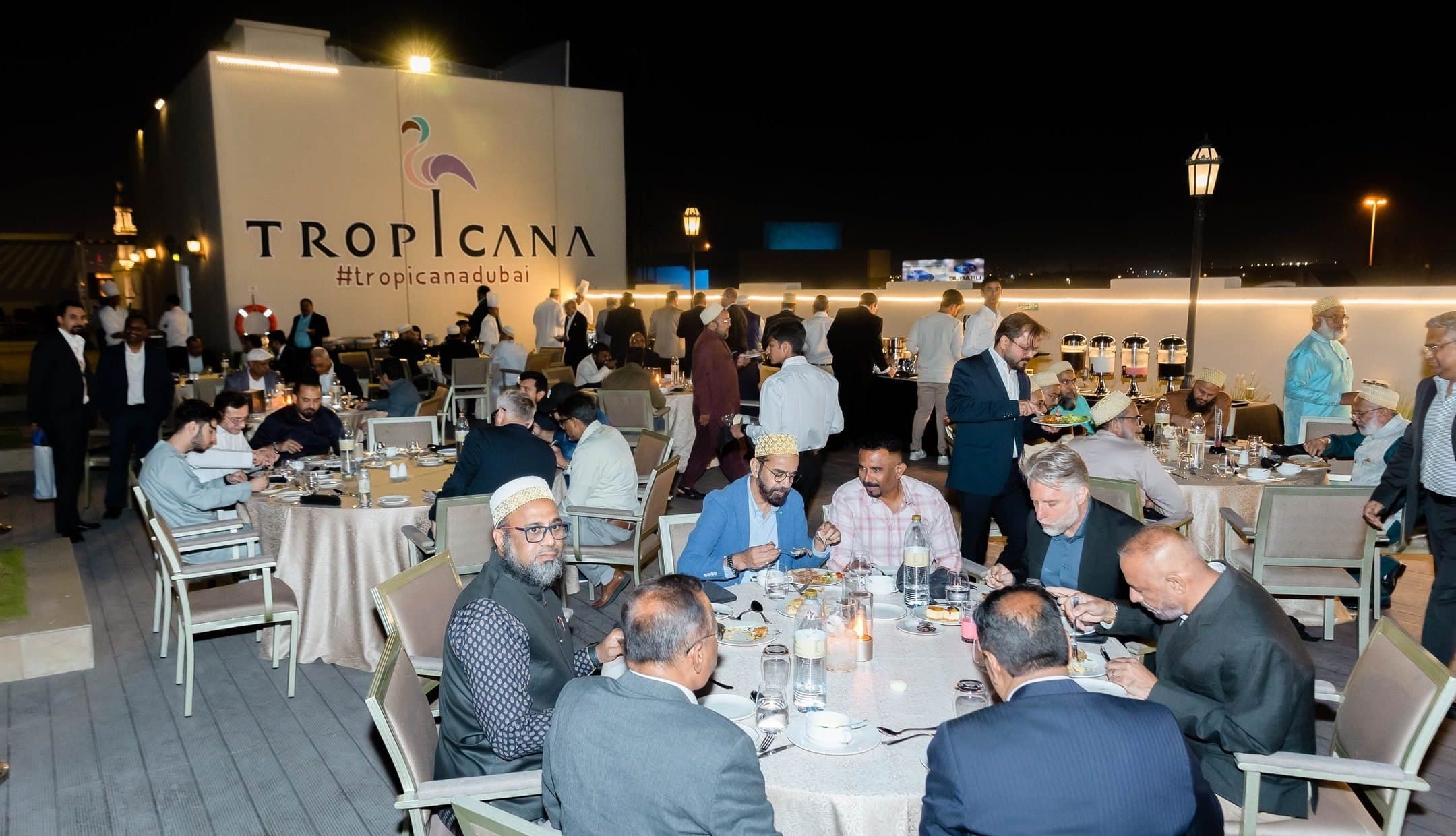 Guests at round dinner tables on a rooftop at night under the Tropicana sign
