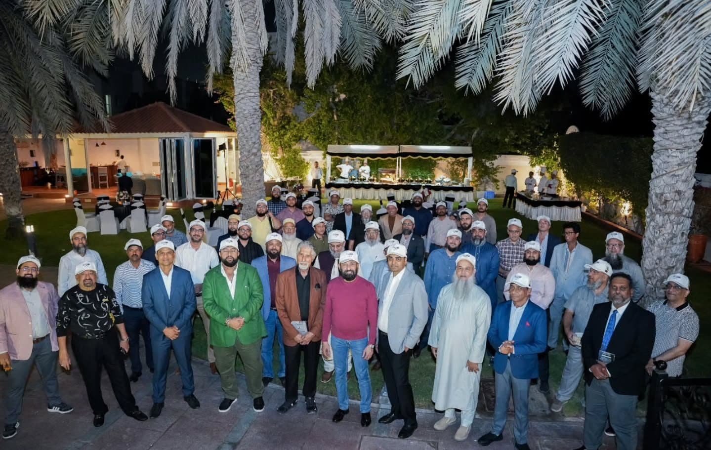 Large group photo at night on a lawn under palm trees