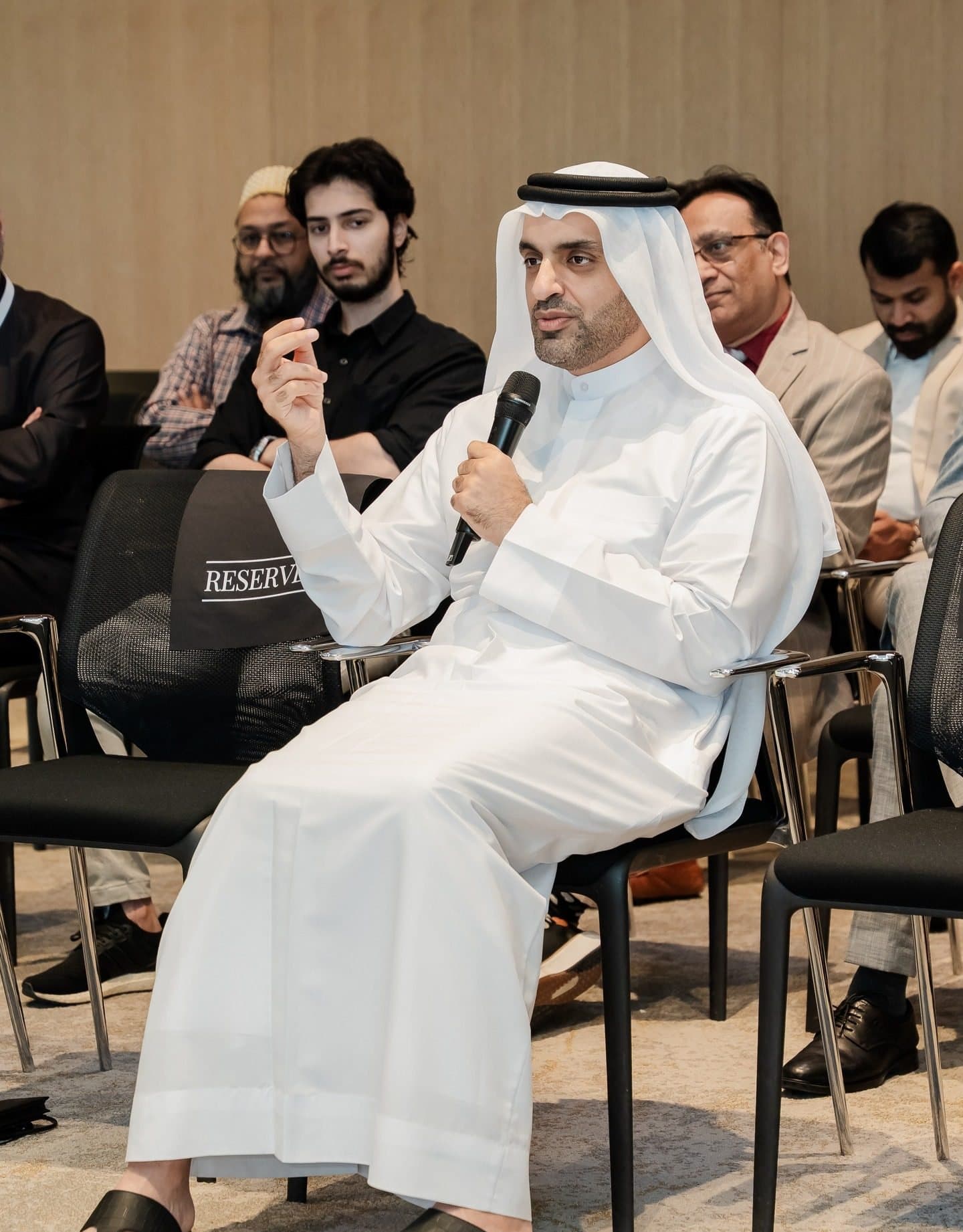 Emirati man in white kandura seated and speaking into a microphone