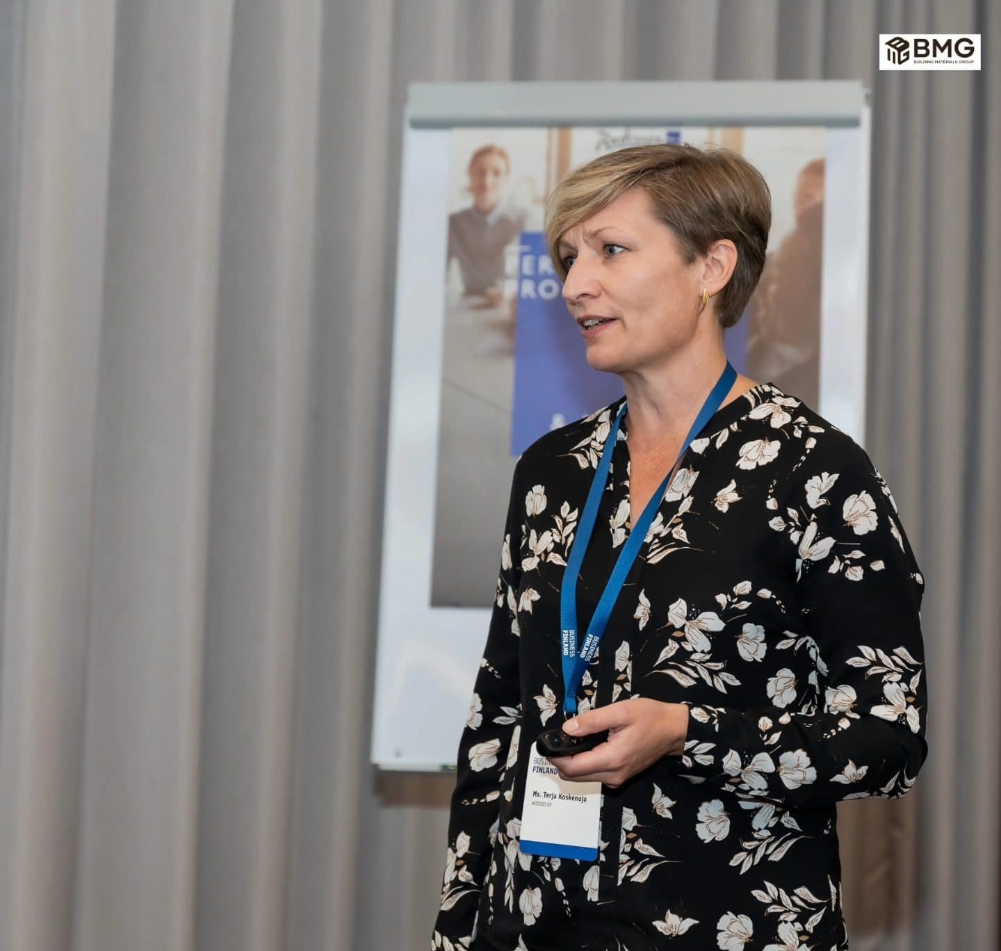 Woman with a conference lanyard speaking to the room, holding notes
