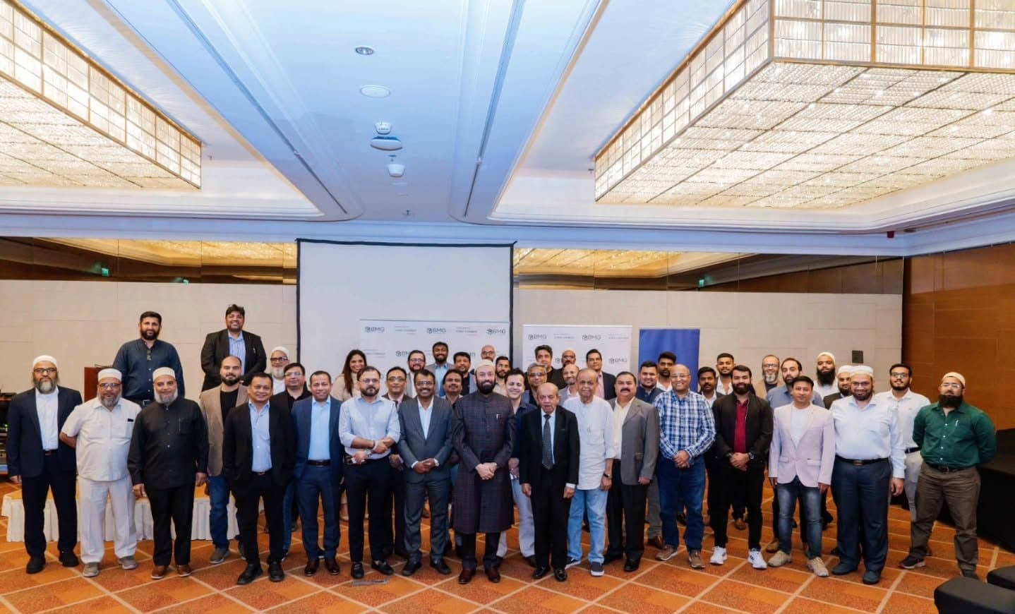 Large group of members posing in a hotel ballroom in front of a projection screen
