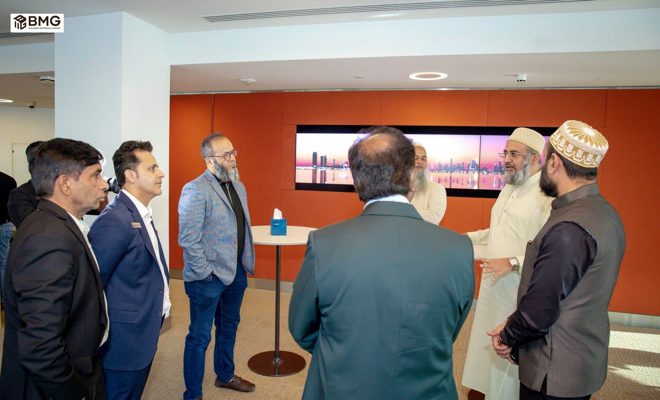 Small groups of men talking in an office space with a city skyline screen behind