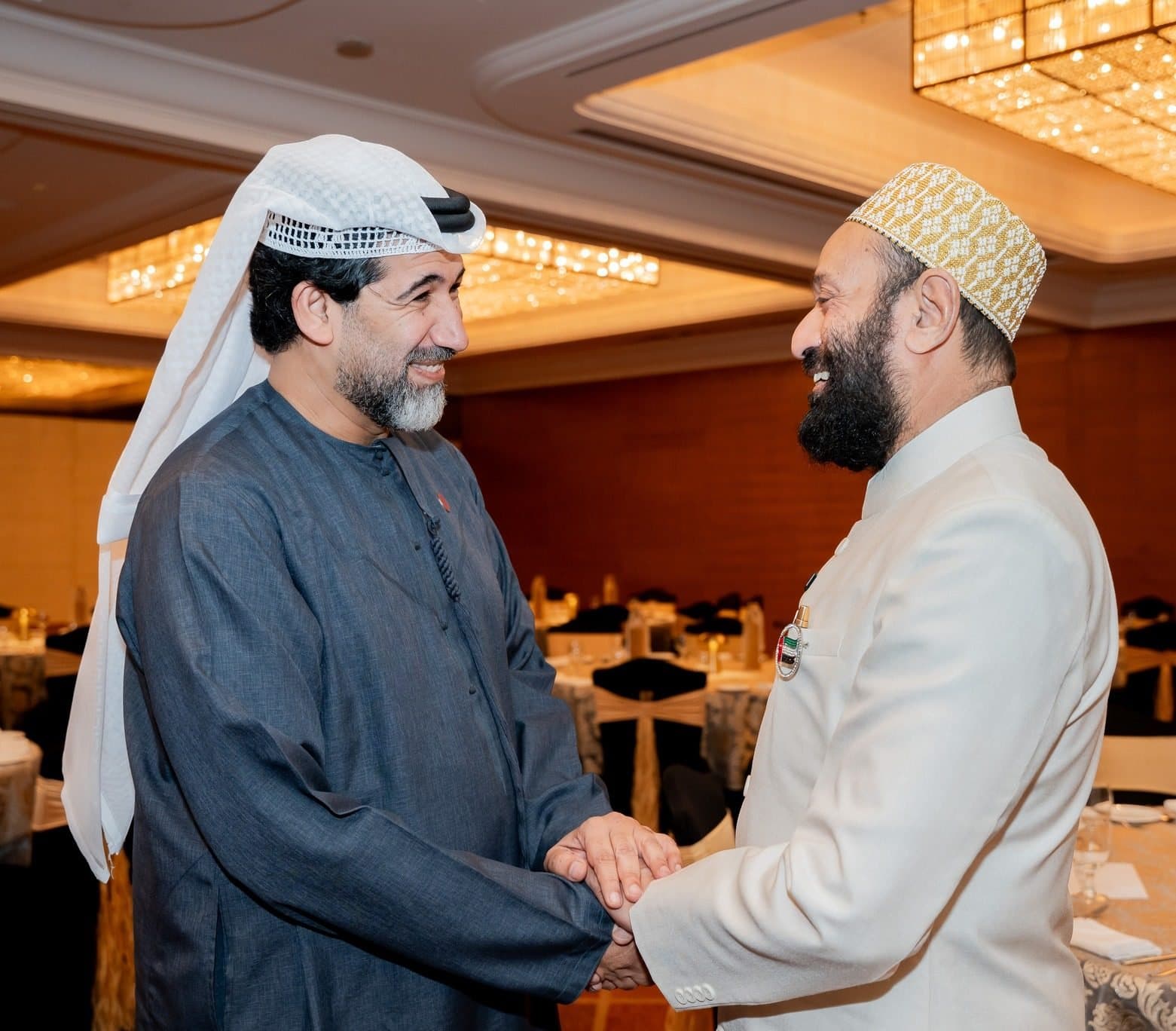 Two men clasping hands in greeting, one in a dark robe, one in a white jacket and cap