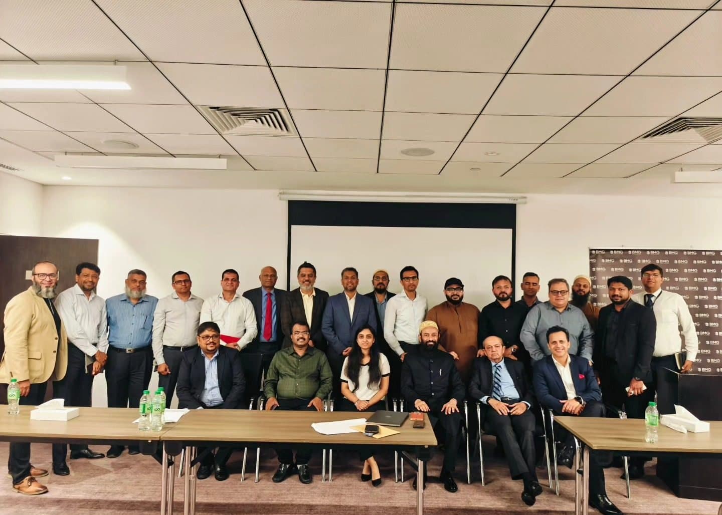 About thirty traders posing seated and standing behind meeting tables in a hotel room