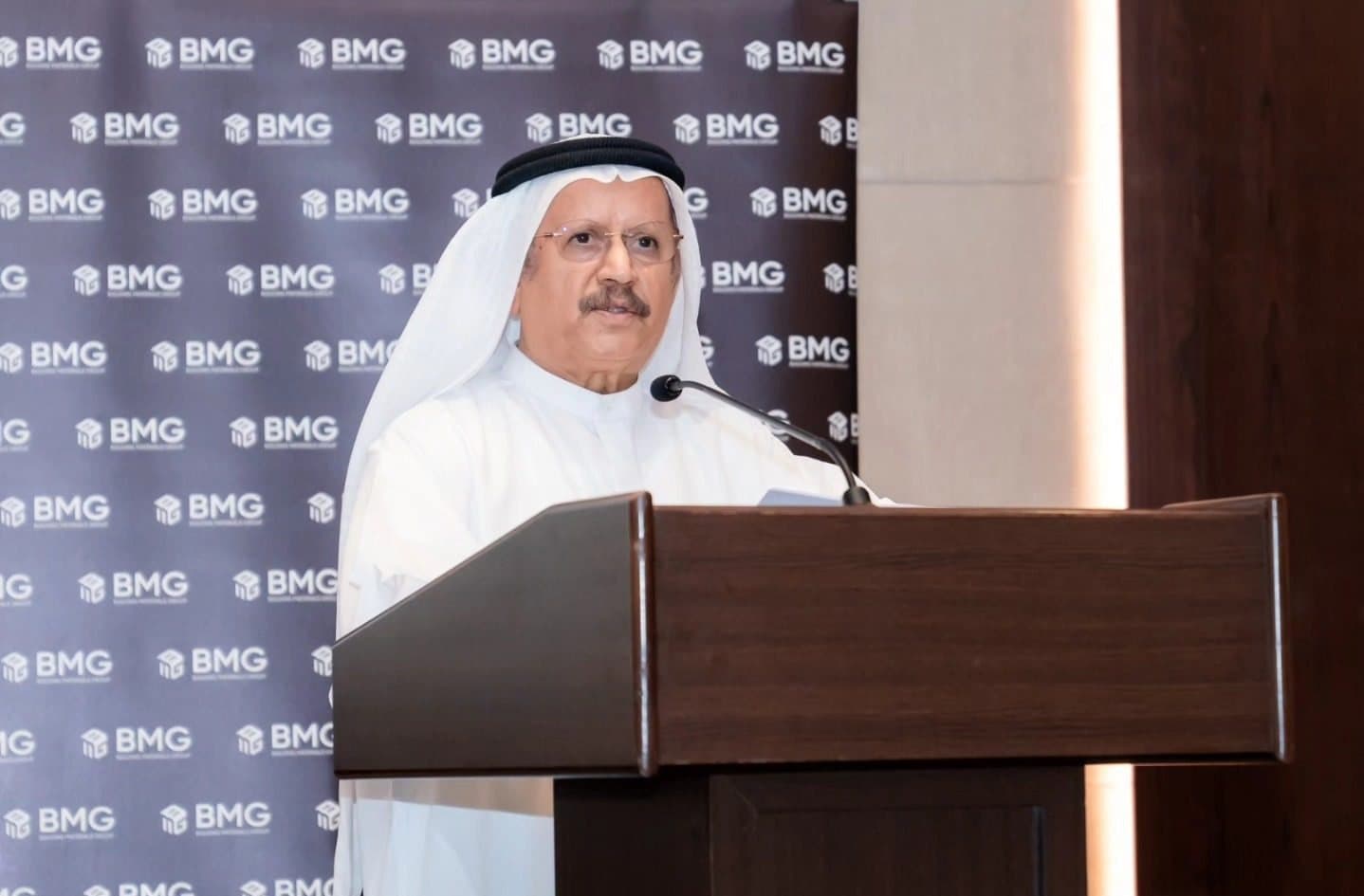 Senior Emirati guest speaking at a podium in front of a BMG logo backdrop
