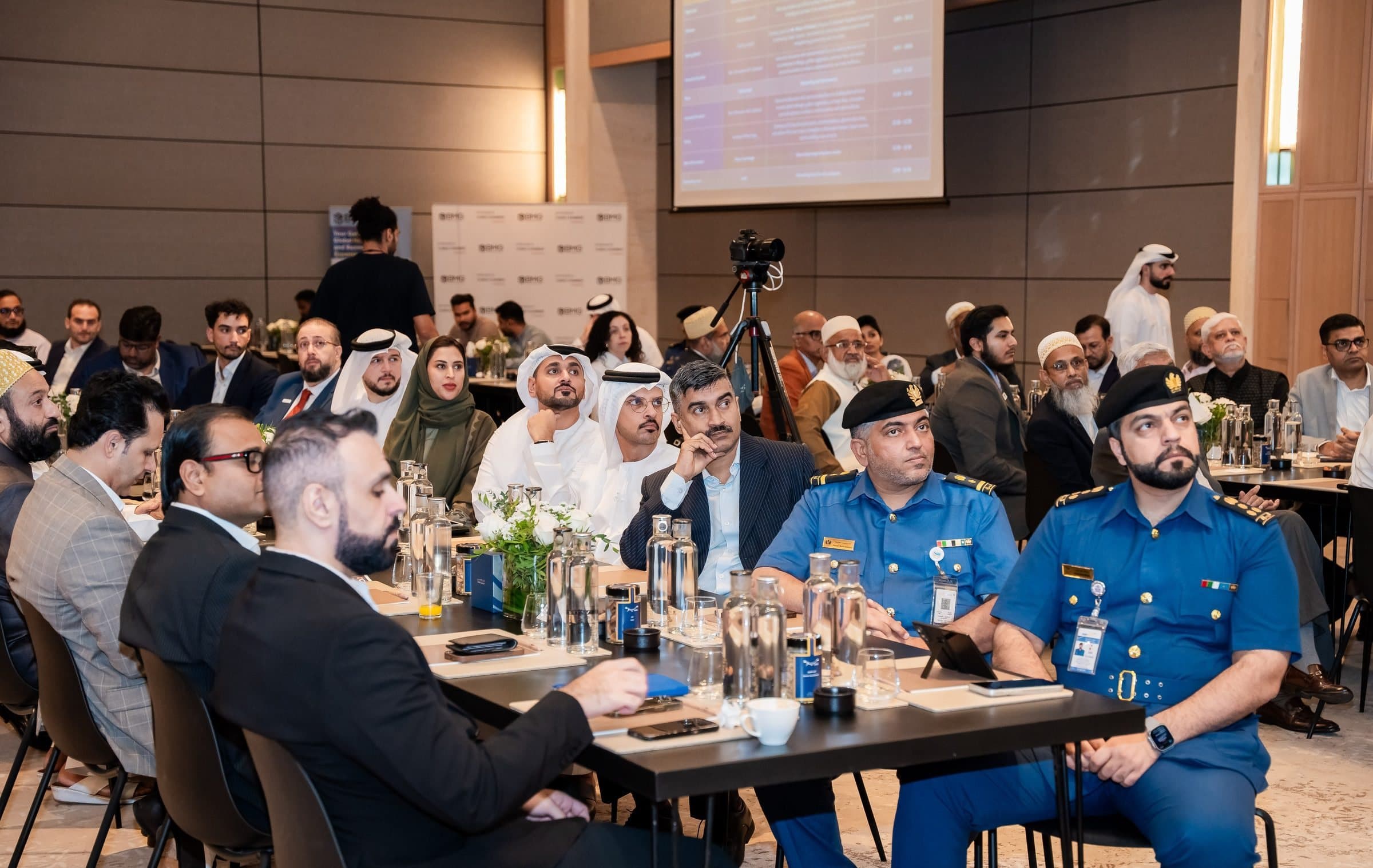 Attendees seated at long tables, including uniformed customs officers